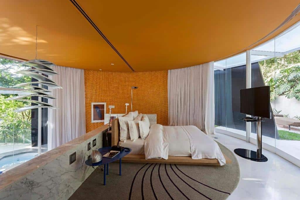 Quarto de luxo do Unique Garden com uma cama de casal, paredes de vidro que dão vista para um jardim, uma televisão e uma piscina privativa