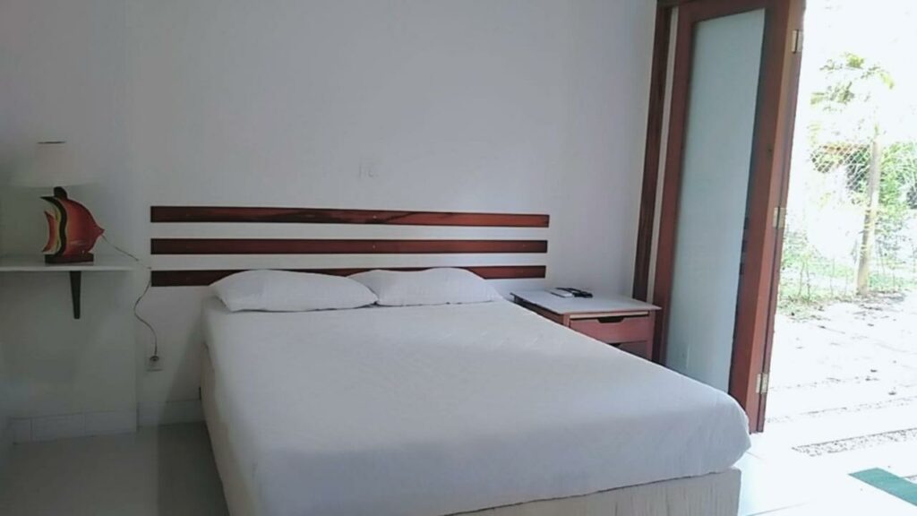 Quarto da Villa Félix Suites e Chalés com cama de casal no centro da imagem e do lado esquerdo uma cômoda do lado da cama. Representa airbnb na praia do Félix.