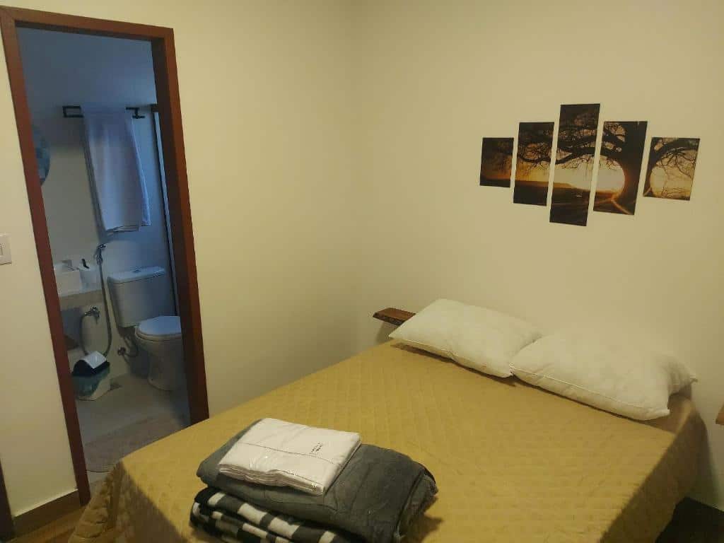 Quarto do Villa Sunset chalés Ibitipoca com uma cama de casal ao centro com travesseiros, uma colcha e um edredom dobrado em cima. Na parede atrás da cama tem um quadro e na parede do lado esquerdo tem uma porta aberta que dá acesso ao banheiro.