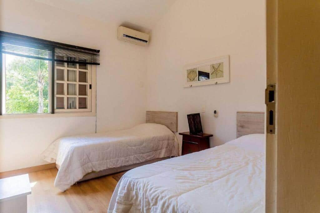 Quarto da Casa em Condomínio Pé na Areia na Praia do Engenho com uma cama de casal a frente, uma cômoda no centro e do lado direito do quarto uma cama de solteiro. Representa airbnb na praia da Juréia.