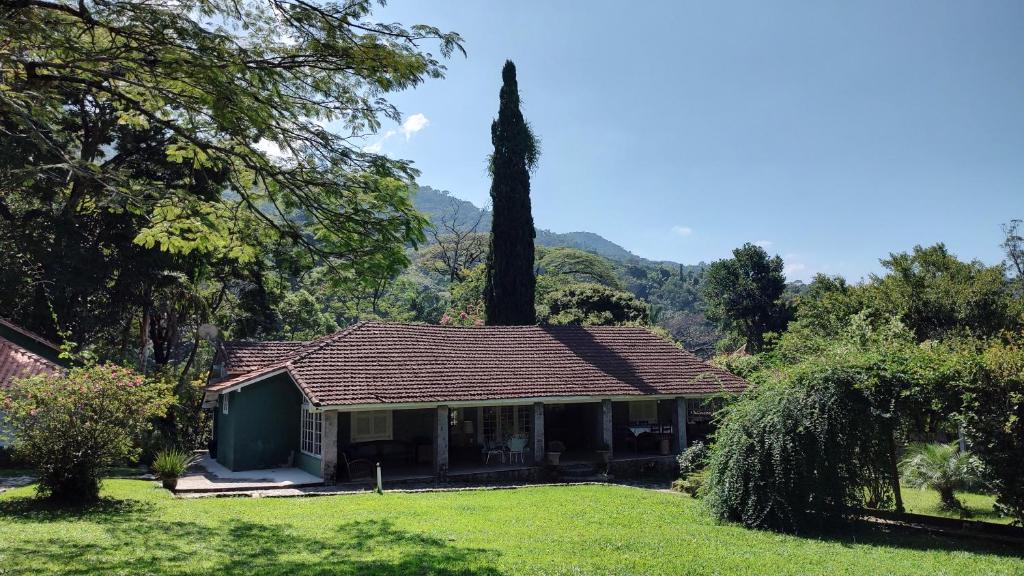 Casa do Rancho São Carlos vista pelo lado de fora. Há uma casa grande no meio da imagem e em volta há árvores e arbustos. Imagem para ilustrar o post airbnb em Itatiaia.