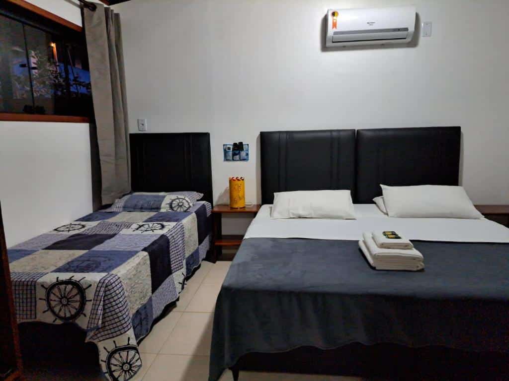 Quarto do airbnb Recanto das Flores Lofts. Uma cama de solteiro está encostada no lado esquerdo do quarto, há um pequeno móvel entre as camas e no lado direito há uma cama de casal. Imagem para ilustrar o post airbnb em Ilha Grande.