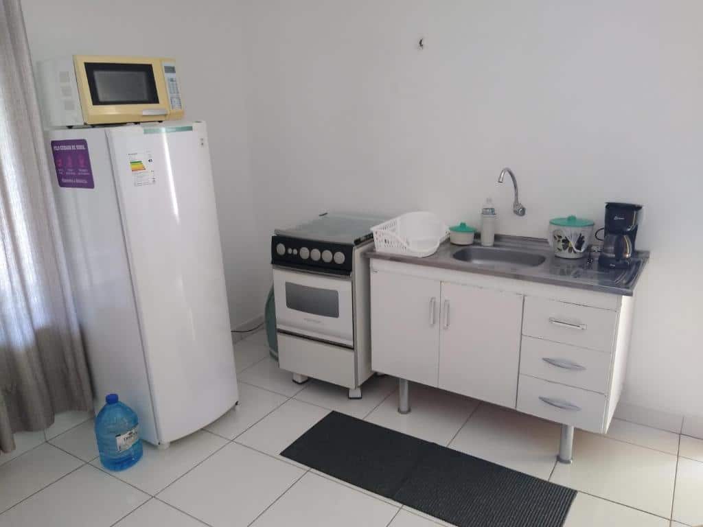 Cozinha com pia ao centro, máquina de fazer café em cima, um fogão no seu lado esquerdo e uma geladeira, também pela esquerda, com micro-ondas em cima em Recanto Só Alegria.