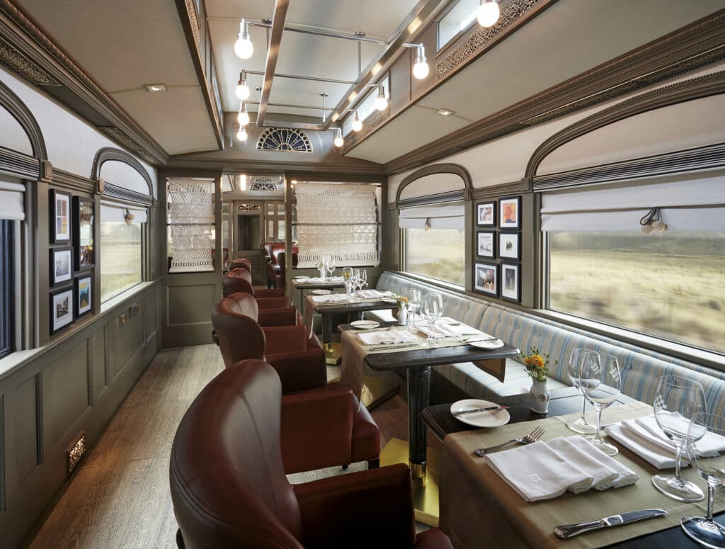 vagão restaurante do andean explorer da perurail com mesas decoradas com taças e pratos, além de uma bela vista nas janelas