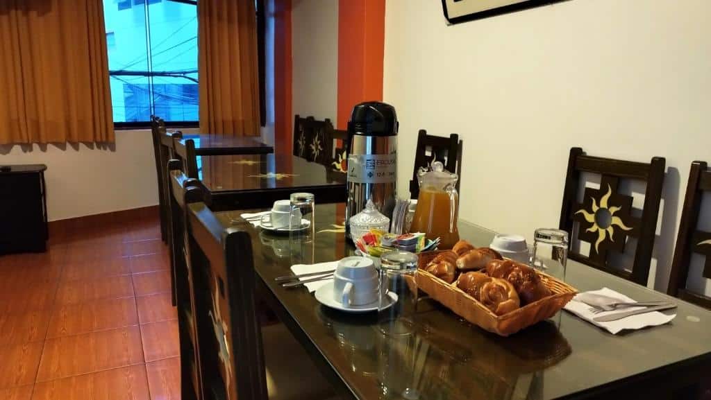 mesa de café da manhã do hotel barato amakonkay machupicchu com uma jarra de pressão de bebida quente, além de pratos de comida e xícaras brancas dispostas em cima da mesa.