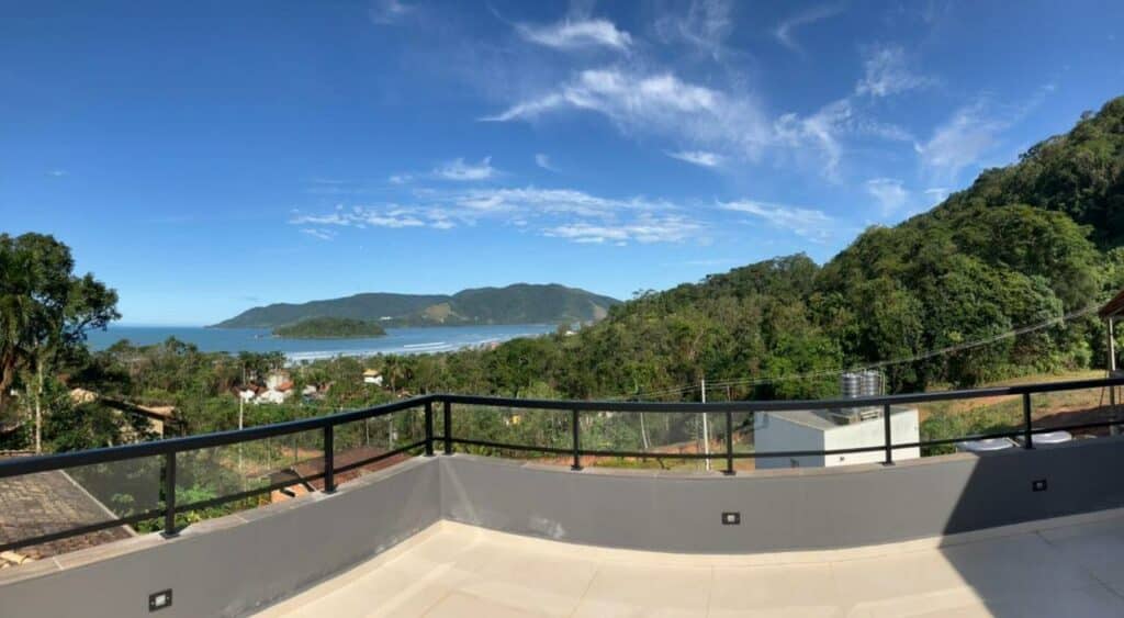 Sacada do Refúgio Praia Lagoinha Ubatuba-SP Condomínio Samola durante o dia com sacada a frente e ao fundo, árvores e o mar. Representa airbnb na praia da Lagoinha.
