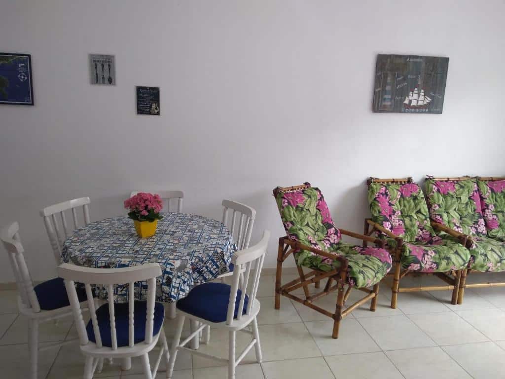 Sala de estar do Apartamento no Tenório com mesa de jantar redonda com seis cadeiras do lado esquerdo da imagem e do lado direito poltronas estofadas.