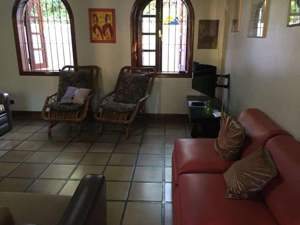 Sala de estar da Casa de Praia a 80 metros da Praia em Ubatuba com sofá do lado direito da imagem do lado direito do sofá uma cômoda com TV e do lado esquerdo ao fundo duas poltronas.