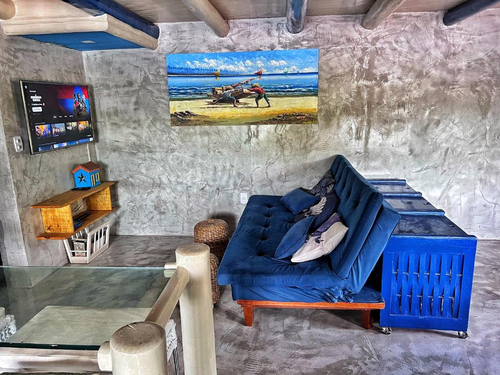 Sala de estar da Casinha Azul Caraíva – casa completa na beira do Rio com sofá-cama a frente em frente ao sofá-cama a TV presa na parede. Representa airbnb em Caraíva.