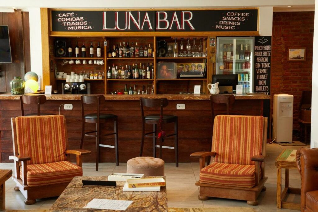 Bar do Hotel Lunajuim com duas cadeiras a frente e ao fundo um balcão com cadeiras e ao fundo o bar.