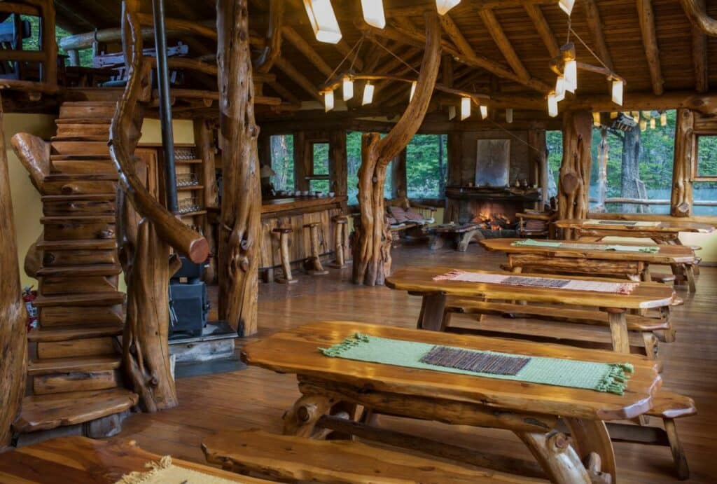Sala de refeição do Laguna Condor – Refugio de Montaña com mesas e cadeiras de madeiras do lado direito.