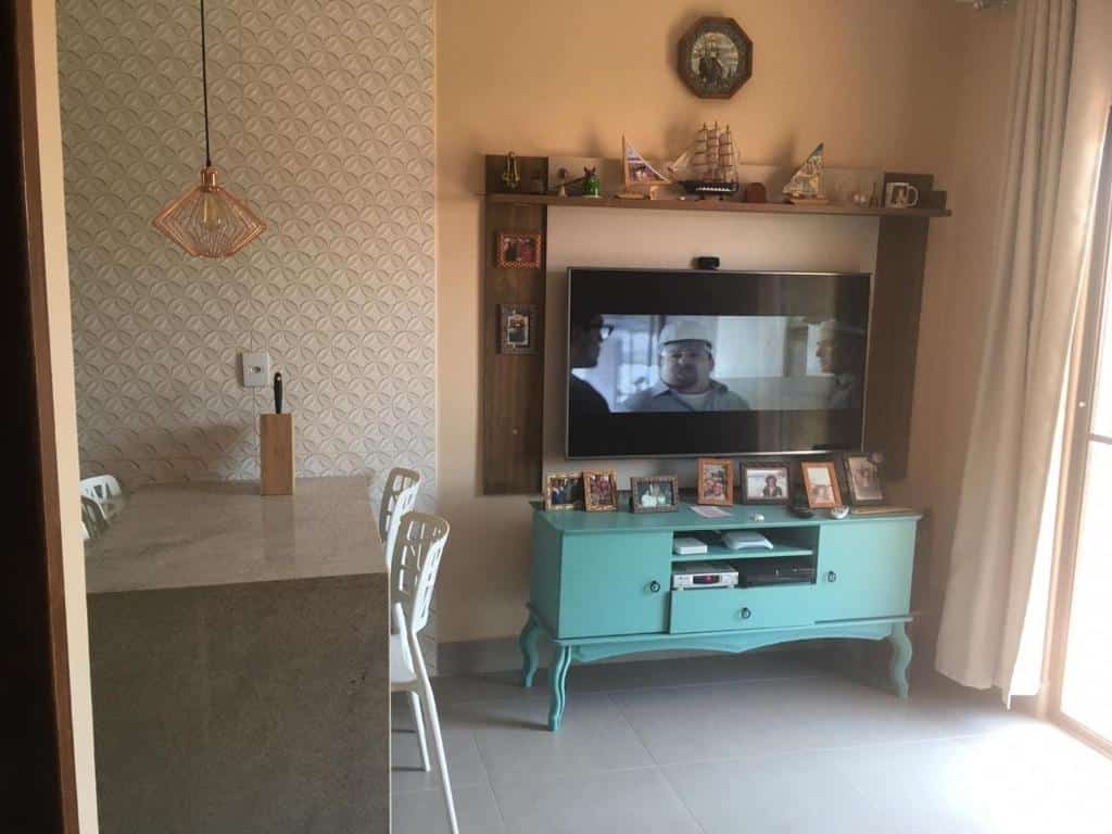Sala de estar do Flat Felicitá Lagoinha com balcão do lado esquerdo da imagem com três cadeiras e do lado direito uma cômoda com TV presa na parede. Representa airbnb na praia da Lagoinha.