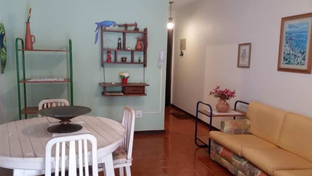 Sala de estar do Ubatuba Tenório apto térreo 6 pess com mesa redonda com três cadeiras do lado esquerdo da imagem a frente e do lado direito da imagem um sofá.
