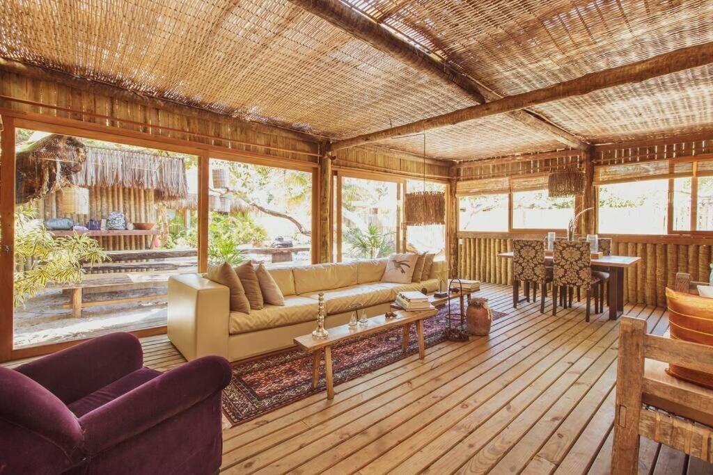 Sala de estar Vila Botanika Caraíva com poltrona do lado esquerdo da imagem a frente um sofá e uma mesa de centro, do lado esquerdo do sofá a frente uma mesa de madeira com quatro cadeiras.