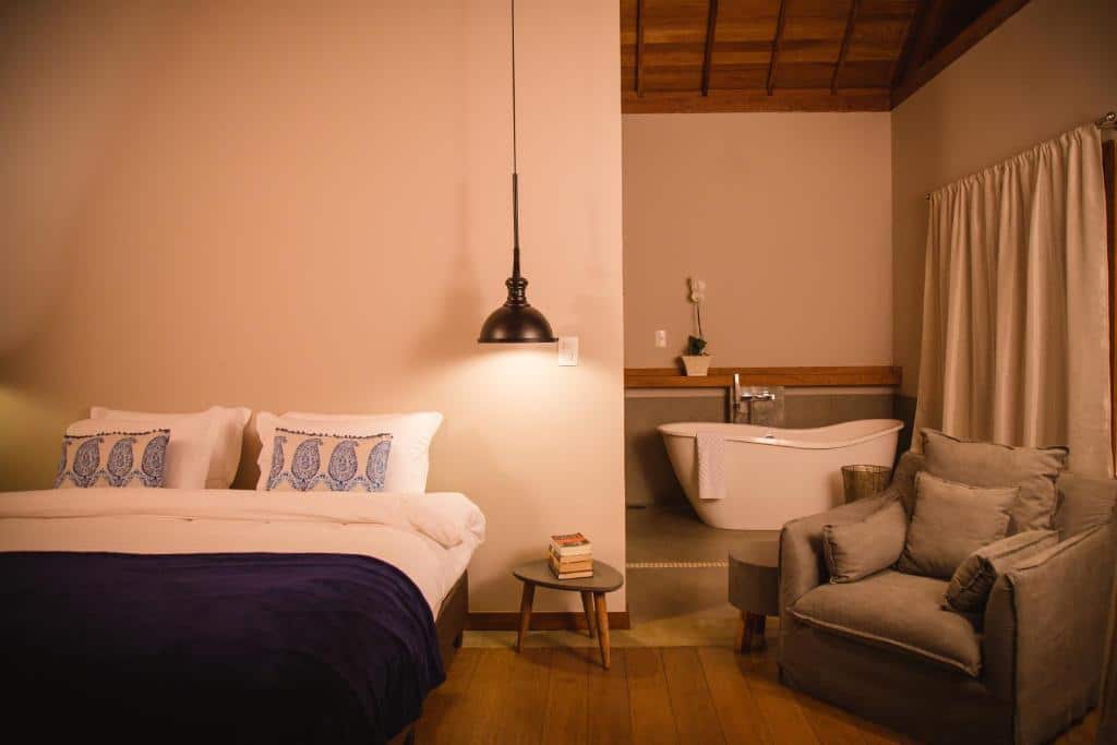 Quarto do Serra do Ibitipoca Hotel de Lazer com uma cama de casal na parte esquerda da foto e do lado direito tem uma poltrona acolchoada e ao fundo uma banheira de hidromassagem. Imagem ilustrando post Airbnb em Ibitipoca.