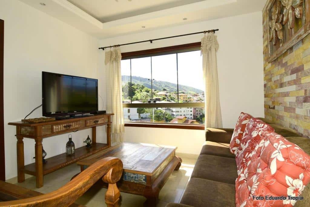 Sala do Solar Douro. Na direita há um sofá, e na frente dele está uma mesa de centro e uma rack com televisão. Ao fundo há uma janela grande com vista.