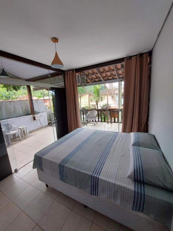 Quarto do Solaris do Una, um dos airbnb em Barra do Una. Uma cama de casal está no centro do local que é cercado por portas de vidro que levam à varanda com móveis externos.