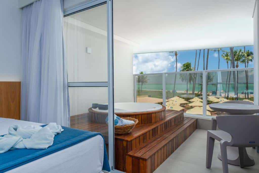 Suíte Dupla Excellence do Maragogi Brisa Excelente Hotel. Na imagem mostra uma parte da cama, com uma varanda com hidro e vista do mar