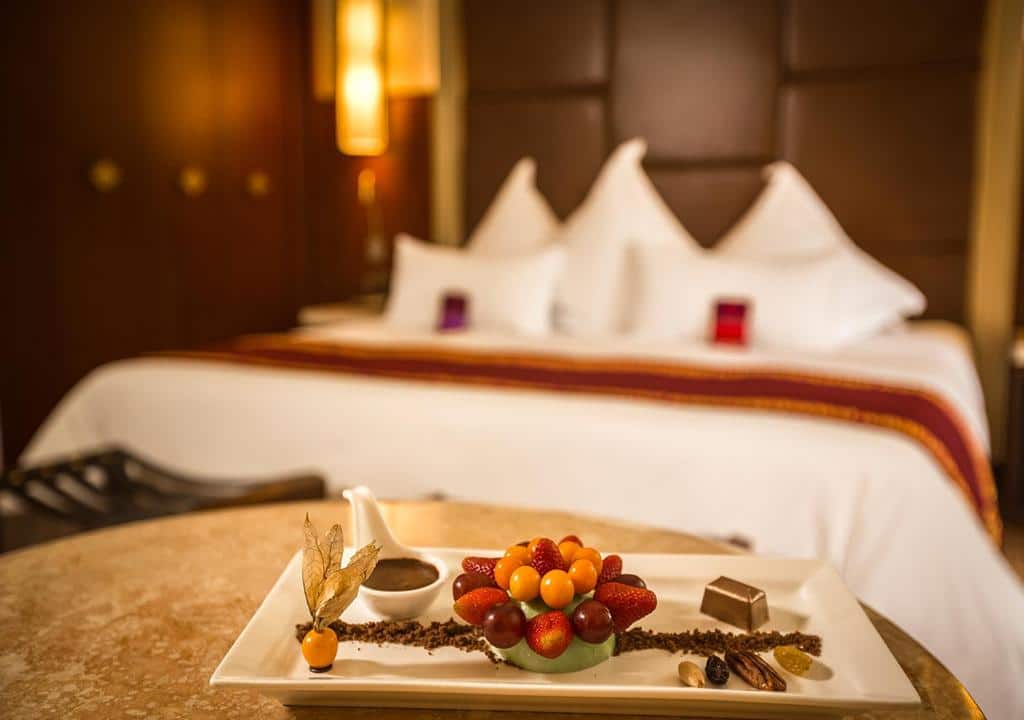 quarto desfocado do Sumaq Machu Picchu Hotel mostrando uma mesa com um prato de frutas e chocolates em frente a uma cama de casal desfocada ao fundo