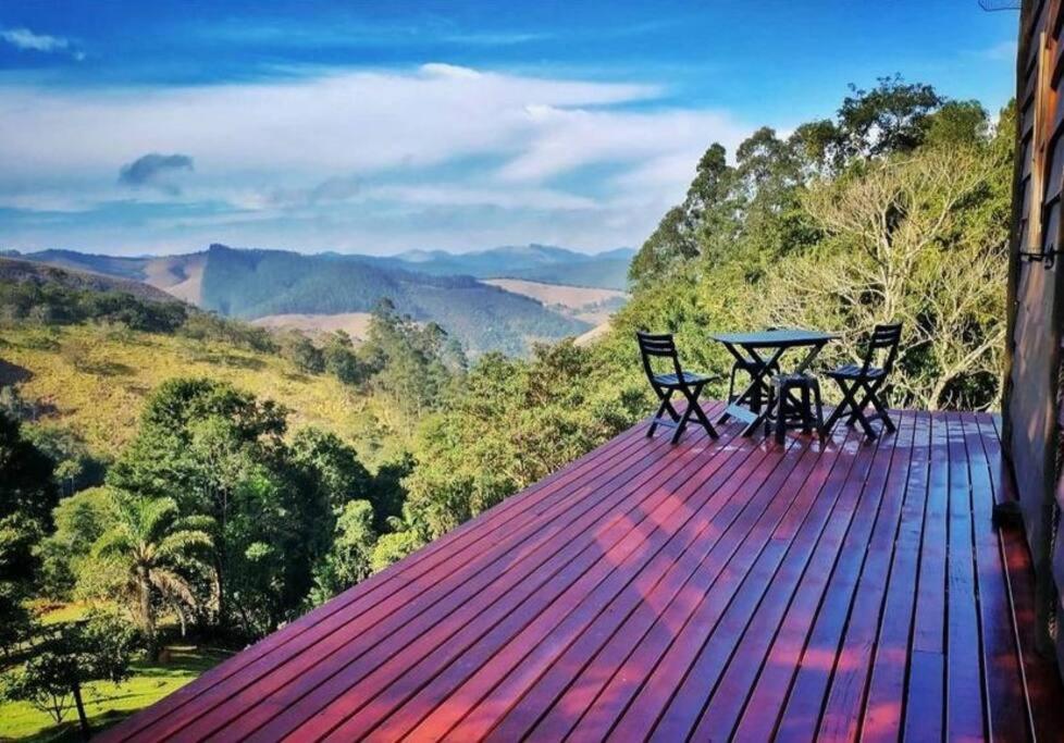 Vista da varanda do Tao da Serra – cabana em meio à natureza!. No canto da varanda há uma mesa com cadeiras. A vista é para a vegetação e montanhas.