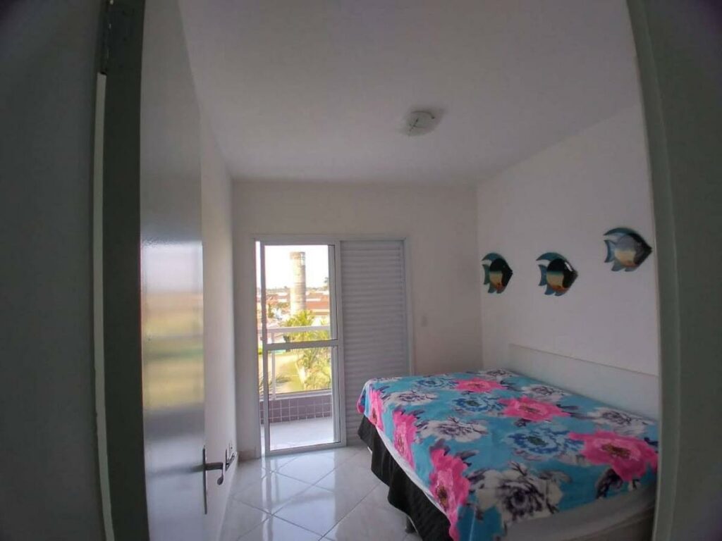 Quarto dos terraços do maitinga, um dos airbnb em Bertioga. Uma cama de casal com jogo de cama está encostada na parede ao lado direito, e uma porta fica ao fundo do ambiente.