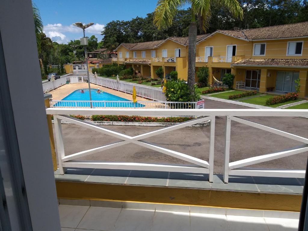 Varanda do Villagio Charmoso na Praia da Mococa durante o dia com vista para a piscina do lado esquerdo da imagem e do lado direito várias casas.
