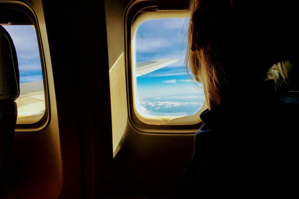 pessoa olhando para  a janela do avião reflexiva em que é possível ver a asa do avião e o céu azul para ilustrar o post de seguro viagem cobre cancelamento da viagem