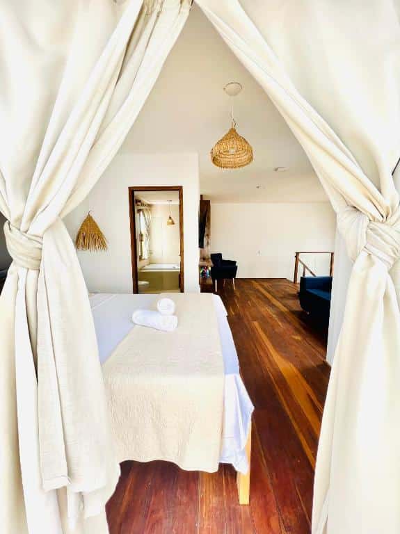Foto do quarto da Villa Mar Residence. Representa o post sobre airbnb em Jericoacoara. Vemos a foto tirada da varanda, mostrando parte do interior do quarto. Uma cortina está na janela, e vemos parte da cama, um banheiro e a escada que leva para o primeiro andar.