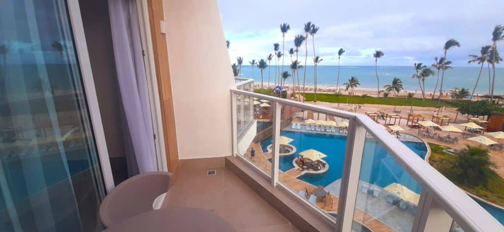 Varanda de um dos quartos do Maragogi Exclusive Hotel com uma mesa redonda e uma cadeira, e vista da área de piscina e praia de Antunes