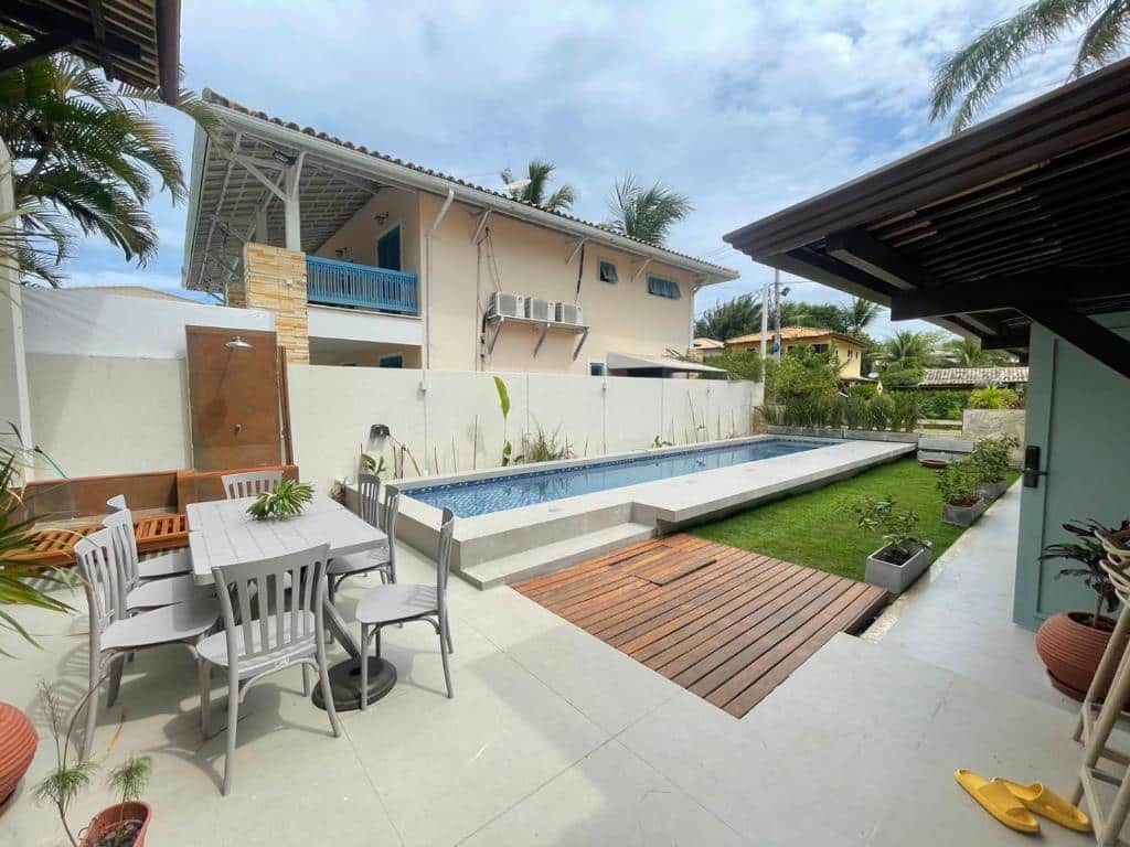 Área de lazer na A CASA DA PRAIA DO FORTE. O quintal possui uma piscina grande, mesa externa com cadeiras, jardim e ducha.