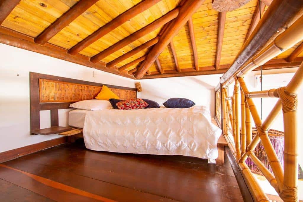 Foto do quarto em Aloha Residence I, que ilustra o post de airbnb na Praia do Forte. A cama está num segundo andar do loft é de casal e há várias almofadas em cima dela.