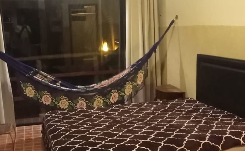 Quarto do Altar da praia Vermelha 180° de vista para o mar. Uma cama de casal está encostada na parede e ao lado de uma rede. Ao fundo está a porta da varanda, airbnb na Praia Vermelha do Centro.