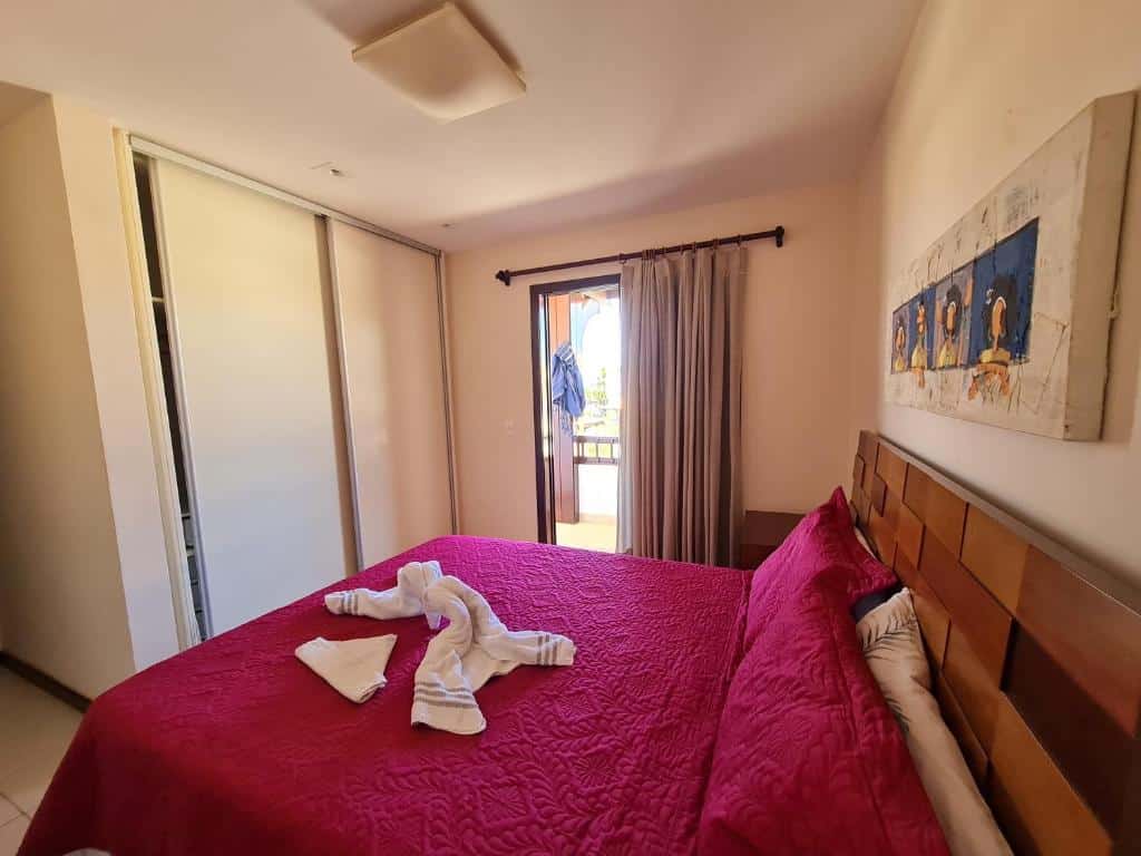 Foto do quarto em Praia do Forte - ap Bali Bahia 107, que ilustra o post de airbnb na Praia do Forte. Vemos a cama de casal de lado. Na frente dela há um guarda-roupa moderno, e do lado há uma porta com varanda.