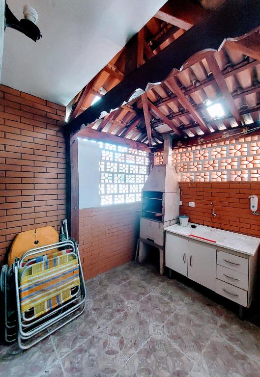 Parte do Apartamento Ubatuba 150m do mar Maranduba que mostra uma churrasqueira e do lado uma pia para lavar louças com um armário embaixo. Em frente tem algumas cadeiras de praia fechadas. As paredes do ambiente é de tijolos e o teto de madeira e telhas. Imagem ilustrando post Airbnb em Maranduba.
