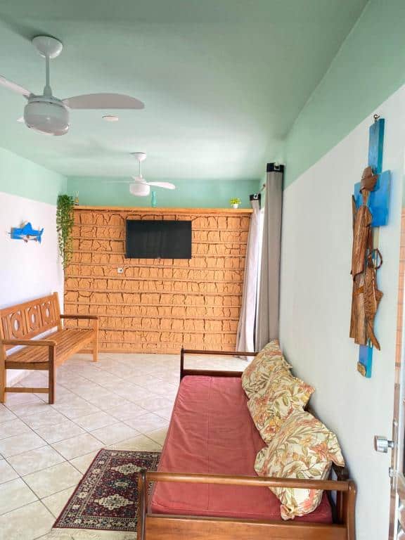 Sala de estar do Aparthouse Beira Mar com um sofá encostado na parede direita e um tapete no chão. Já na parte esquerda tem um banco de madeira e do lado na parede ao fundo tem uma tv.
