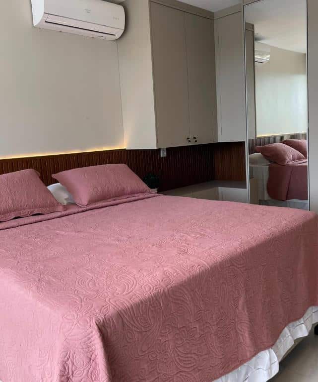 Foto do quarto em Apartamento Alto Padrão 3 quartos Iberostate, que ilustra o post de airbnb na Praia do Forte. Há uma cama box de casal e na sua direita há um guarda-roupa espelhado. No topo da parede acima da cama há um ar-condicionado.