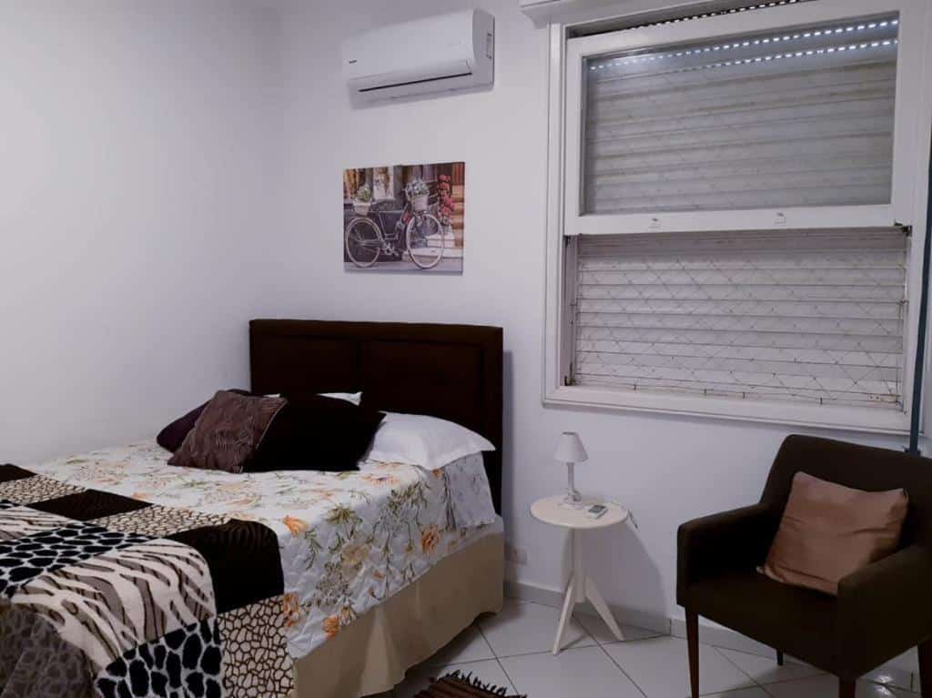 Imagem do quarto do  Apartamento Alto padrão de Frente para o mar, ilustrando o post sobre airbnb em Guarujá. A cama de casal está na esquerda e do seu lado à direita há uma poltrona. Atrás há uma janela