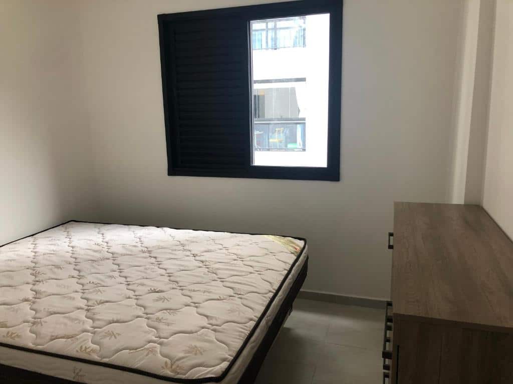 Imagem do quarto do APTO CHURRASQUEIRA, ilustrando o post sobre airbnb em Guarujá. Na esquerda há um colchão e na direita uma cômoda. Na parede do fundo há uma janela. 