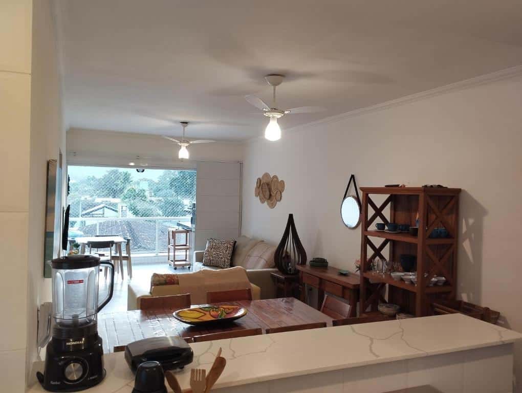 Apto com ar-cond e piscina. Uma bancada, atrás a mesa, cristaleira, cômoda e a sala de estar. Foto para ilustrar post sobre airbnb na Praia da Enseada.