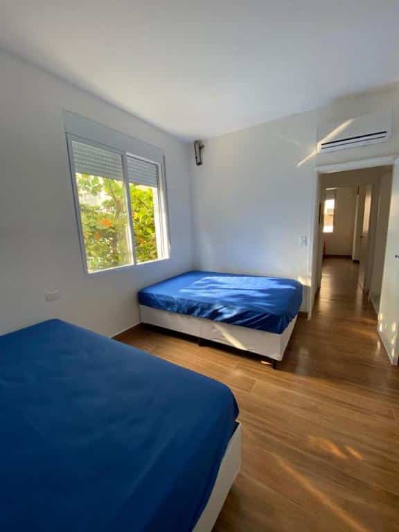 Imagem do quarto do  Apartamento Guarujá Pitangueiras, ilustrando o post sobre airbnb em Guarujá. Há uma cama box de casal no canto inferior esquerdo e outra no fundo à esquerda. Há um ar-condicionado em cima da porta do quarto. A janela está na esquerda.