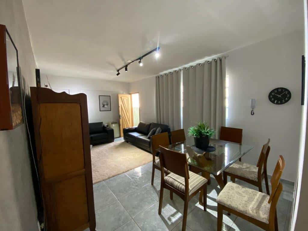 Vista da sala de jantar e de estar do Apartamento VIP Centro Serra Negra. Há uma mesa de jantar com seis cadeiras na direita e mais ao fundo do espaço, à esquerda, estão os sofás na sala.