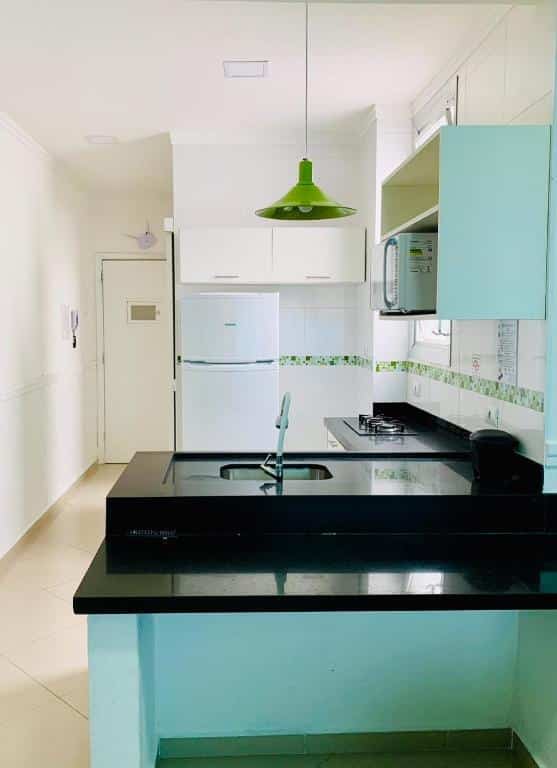 Cozinha no Apartamentos no Guarujá. Há uma bancada, uma pia, fogão cook-top, geladeira, micro-ondas e armários.