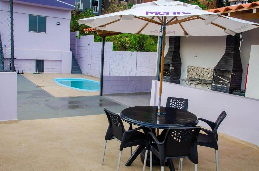 Imagem da área de estar do Studio 900m do centro com uma mesa redonda com quatro cadeiras e do lado direito área de churrasqueira e ao fundo piscina.