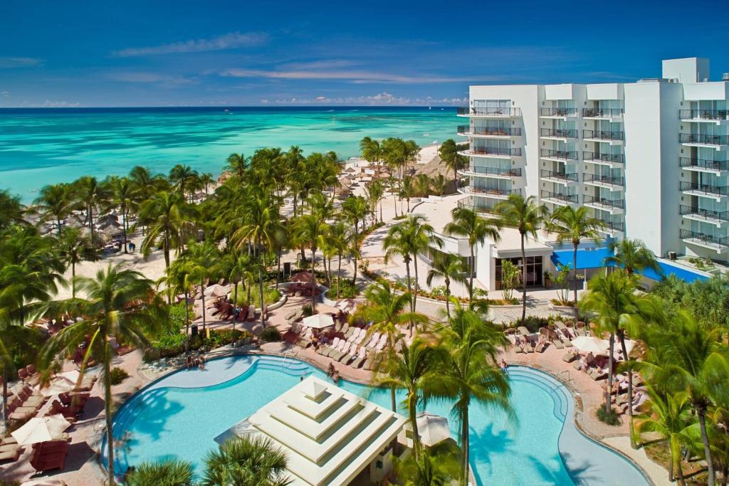 Vista da área externa do Marriott Resort & Stellaris Casino. Uma piscina no meio com palmeiras, no fundo o hotel e o mar.