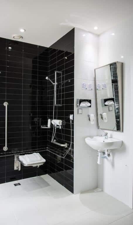Banheiro adaptado do Holiday Inn Express Lisboa com um box sem vidro com um local para sentar-se e barras de apoio, a pia é baixa e sem móvel embaixo