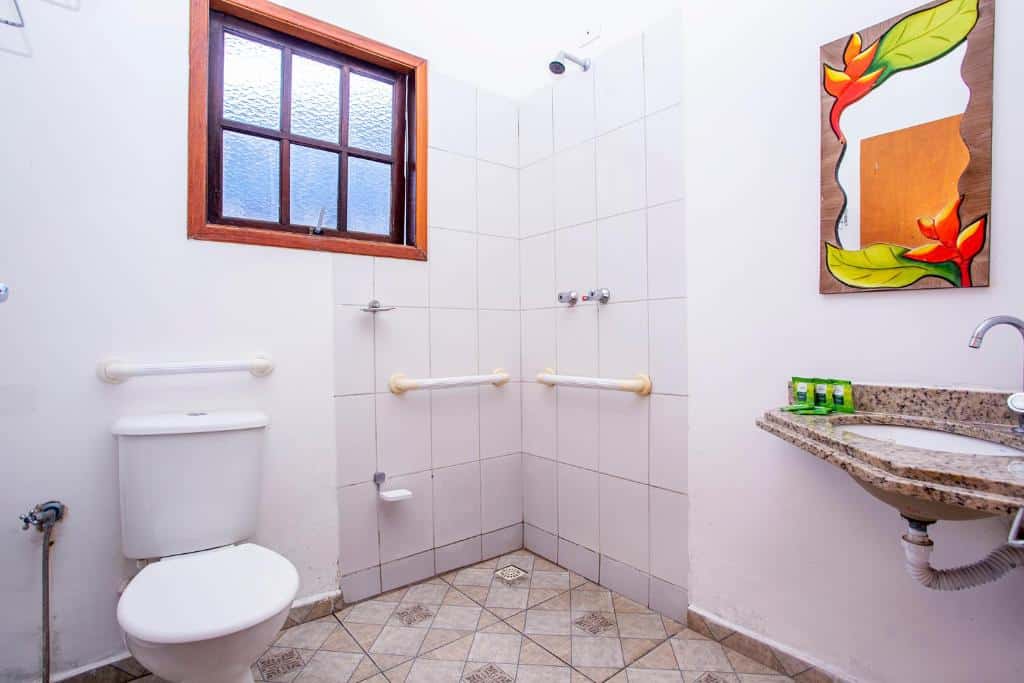 Banheiro com acessibilidade da Pousada Vila Barequeçaba com vaso sanitário do lado esquerdo da imagem com barra de apoio do lado direito chuveiro com barra de apoio.