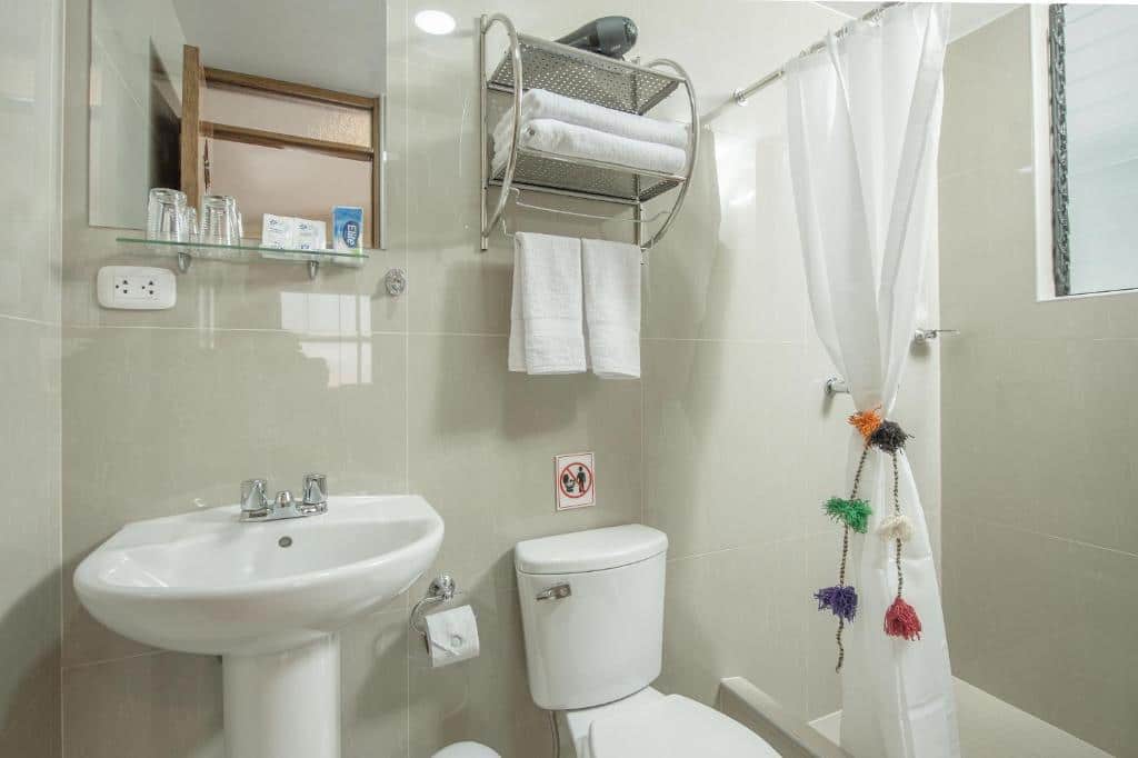 banheiro simples da Casa Matara Boutique com uma pia e um vaso sanitario brancos, e uma cortina de banho branca dividindo a área do chuveiro do restando do espaço.