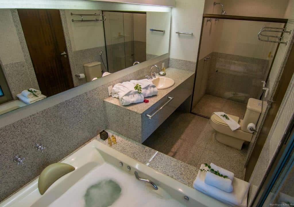 Banheiro com acessibilidade do Garden Hill Hotel e Golfe com banheira do lado esquerdo da imagem no centro uma pia com barra de apoio e em frente a pia o vaso com barra de apoio a cima.