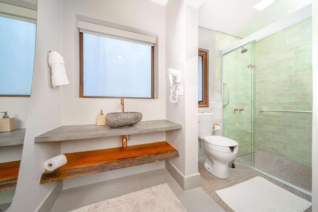 Banheiro com acessibilidade do Øko Villa com pia do lado esquerdo da imagem e do lado direito vaso sanitário e área do chuveiro com barras de apoio.
