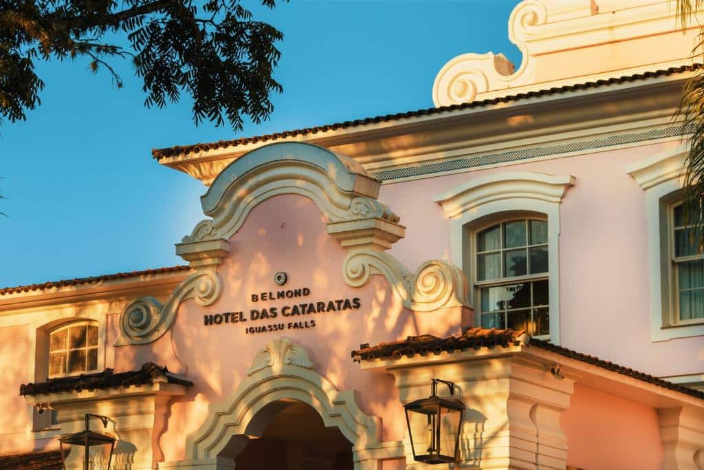 Foto da fachada do Belmond Hotel das Cataratas. Possui uma arquitetura clássica e as paredes são em tom de rosa pastel.